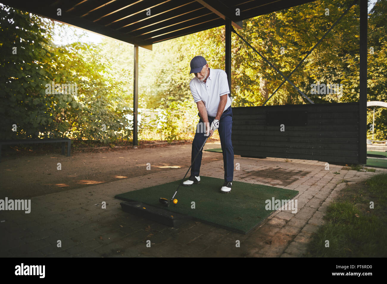 Senior deportivo hombre de pie en una t que practique su swing de golf en un driving range en un día soleado Foto de stock