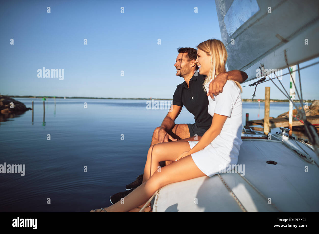 Laughing pareja joven a divertirse y disfrutar de las vistas al océano mientras están sentados juntos en la cubierta de su barco Foto de stock