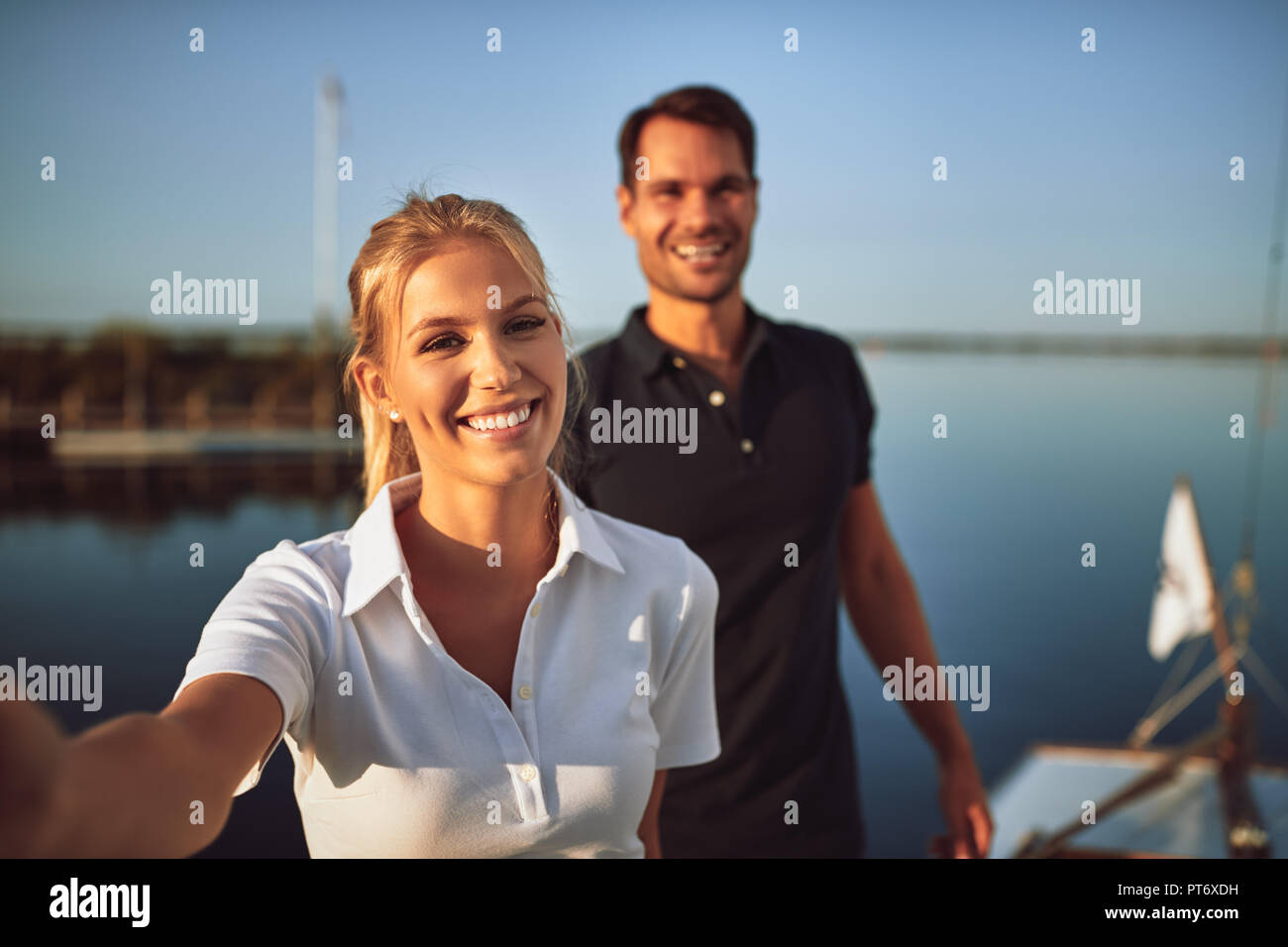 Pareja joven sonriente juntos sobre la cubierta de un barco mientras disfruta de un día soleado vela Foto de stock