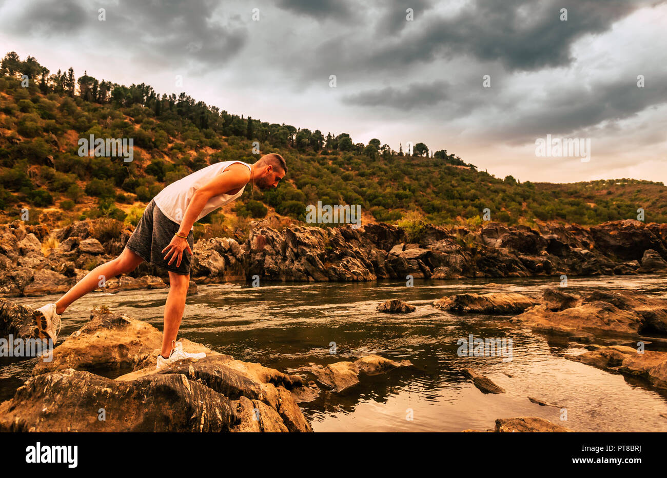 Joven con ropa deportiva en un pie en la cima de la roca del río Fotografía  de stock - Alamy