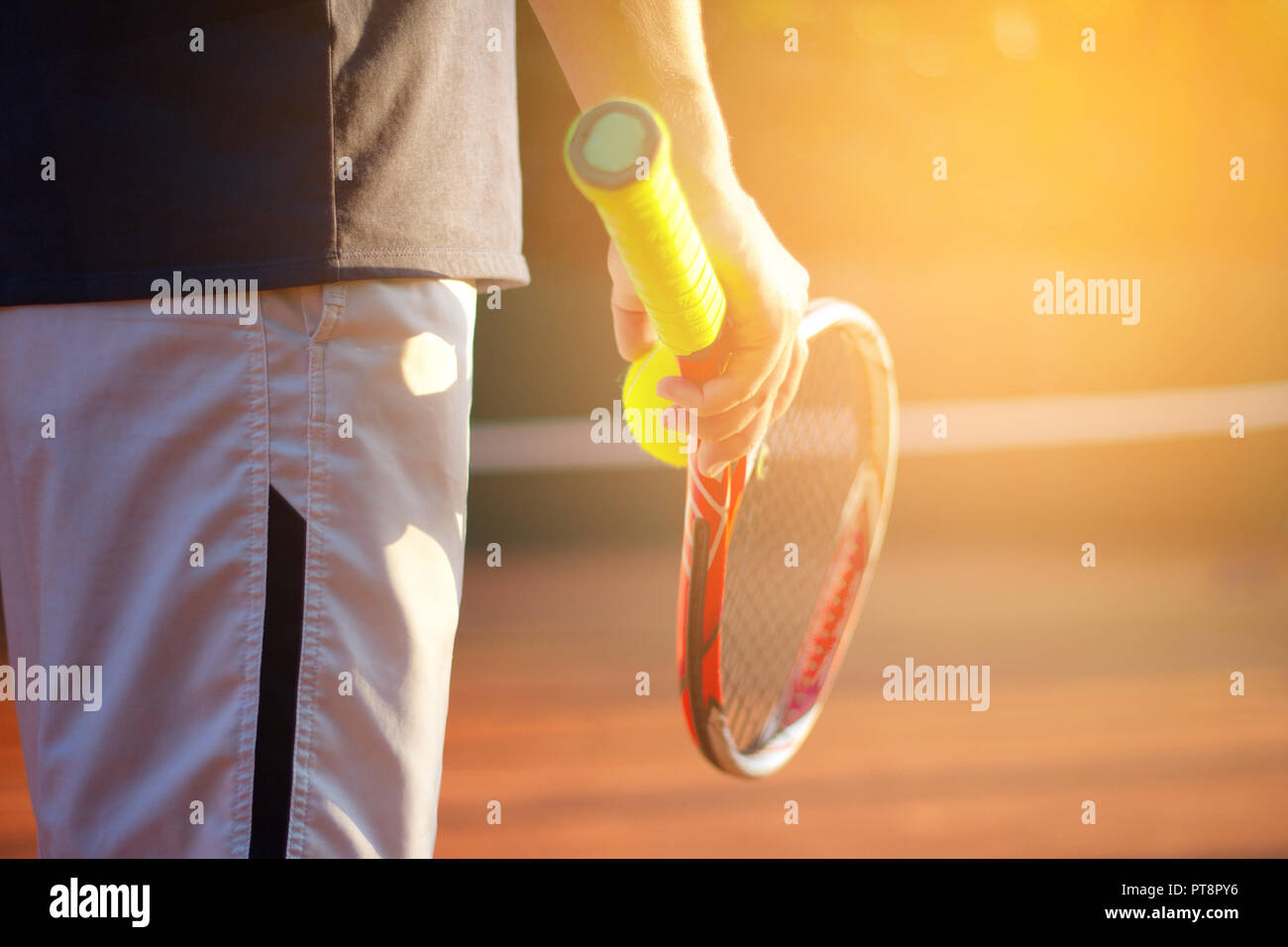 Un jugador de tenis se prepara para servir una pelota de tenis durante un partido na dhold el balón con cohete en la mano derecha. La luz del sol en segundo plano. Foto de stock
