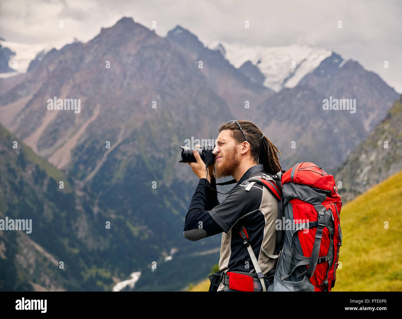 Hombre fotógrafo con gran mochila y cámara tomando fotos de las montañas. Concepto de estilo de vida de viajes de aventura al aire libre vacaciones activas Foto de stock