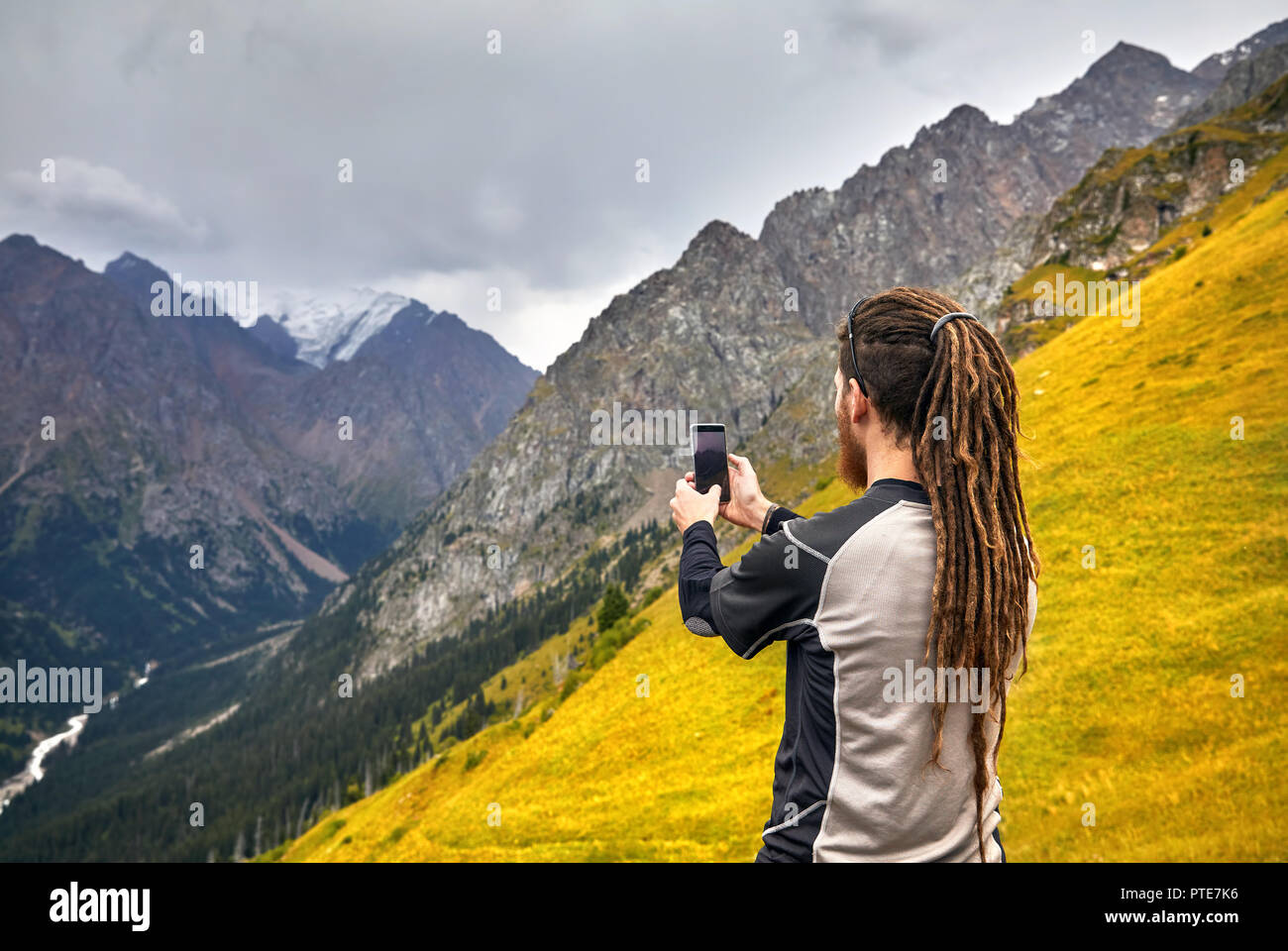 Hombre con dreadlocks tomando fotos con su teléfono en las montañas. Concepto de estilo de vida de viajes de aventura al aire libre vacaciones activas Foto de stock
