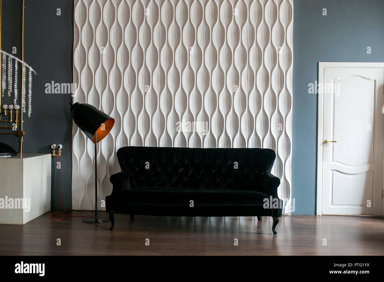 Un sofá negro y una lámpara de piso negro contra una pared en relieve blanco en el espacio loft Foto de stock