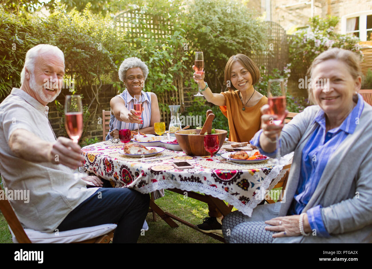 Retrato sonriente, seguros de altos funcionarios amigos bebiendo vino rosado y disfrutando de la comida en la mesa del patio Foto de stock