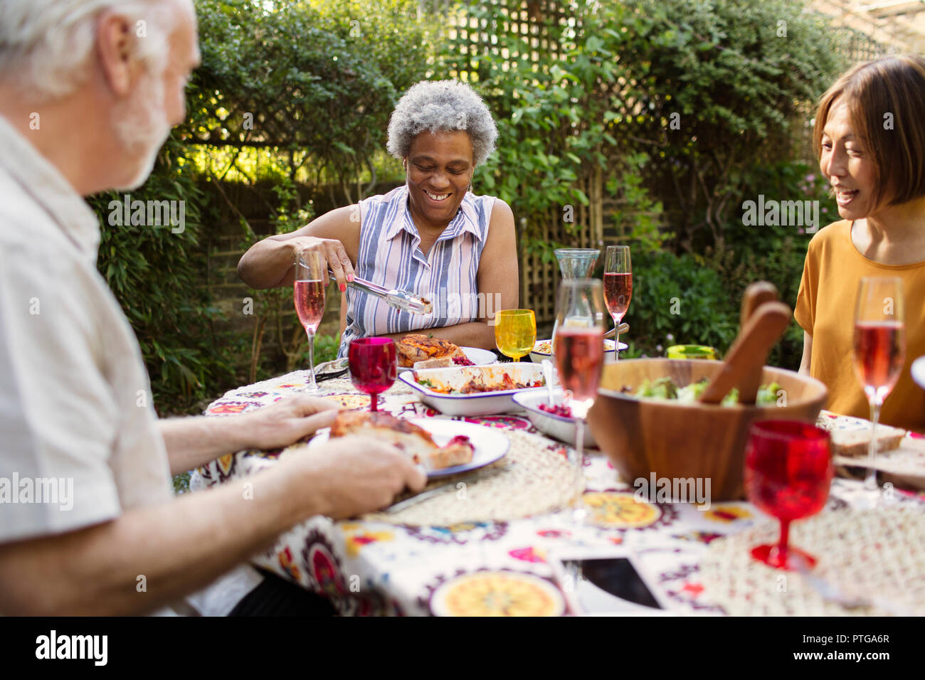 Altos amigos disfrutando de la comida en la mesa del patio Foto de stock