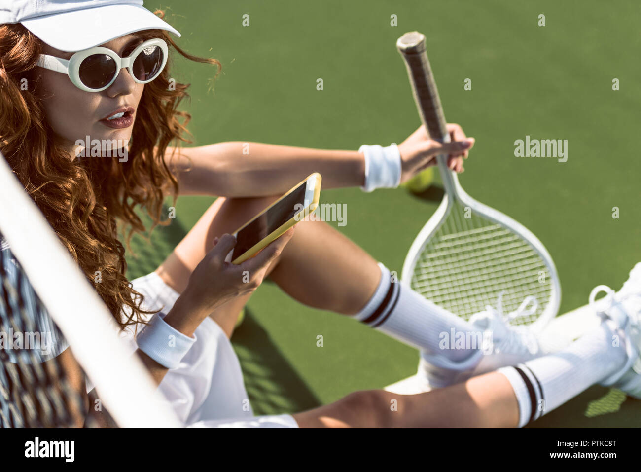 Vista lateral de la hermosa elegante jugador de tenis con smartphone descansando sobre una pista de tenis Foto de stock