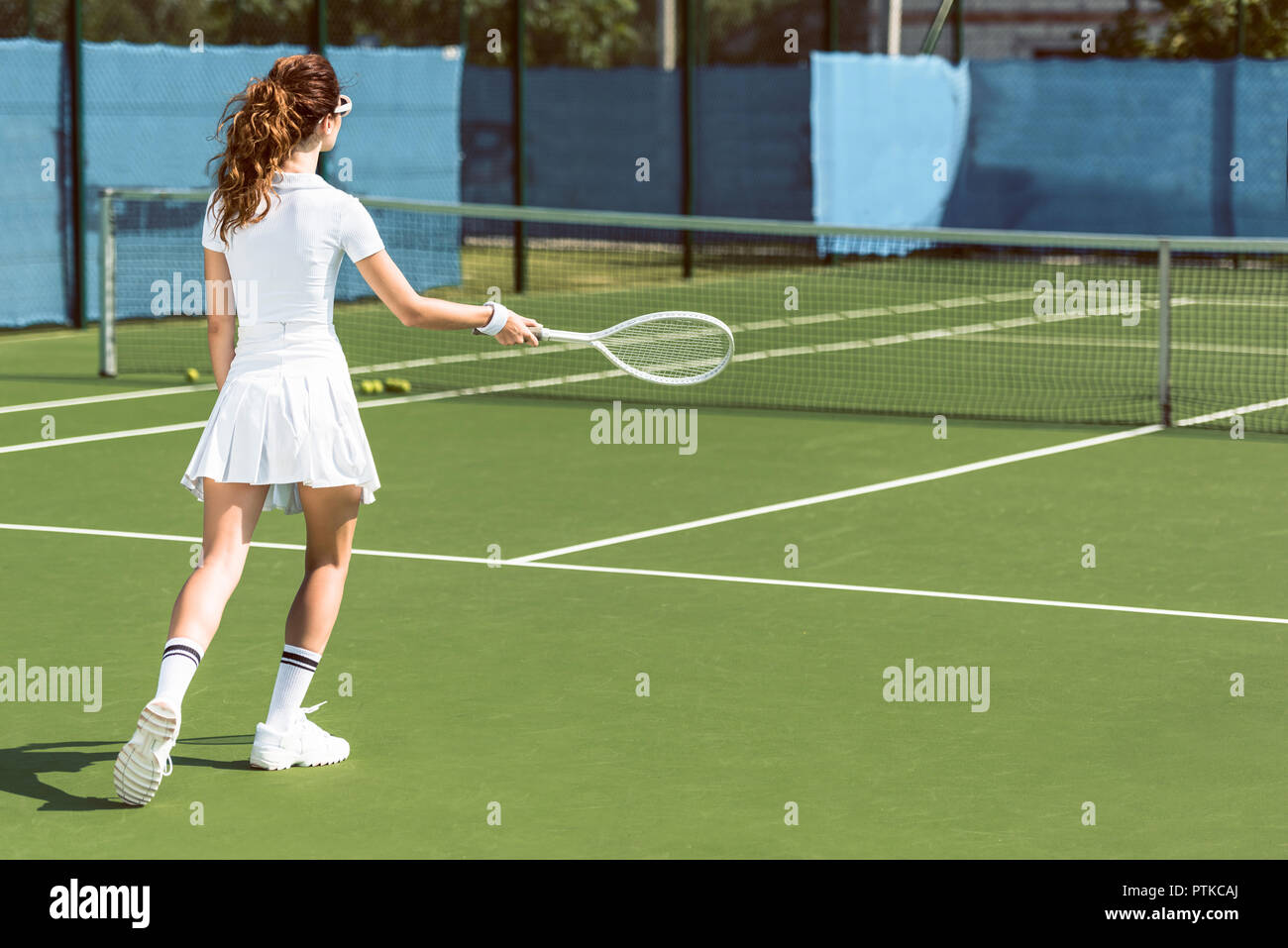 Vista posterior de la mujer en blanco uniforme de tenis jugar al tenis en la cancha Foto de stock
