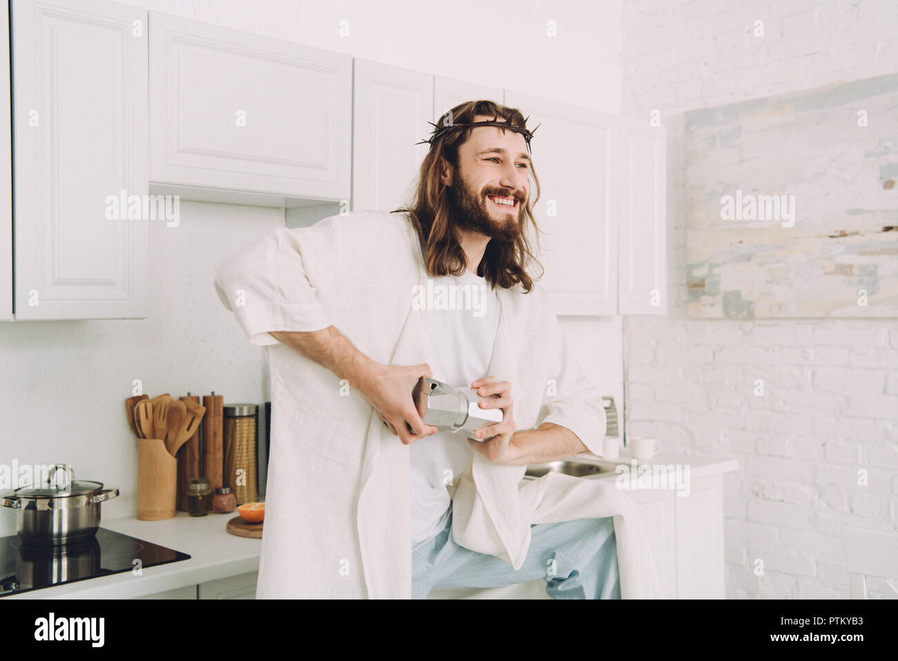 Jesús sonriente moliendo granos de café con las manos en el manual coffeemill en cocina en casa Foto de stock