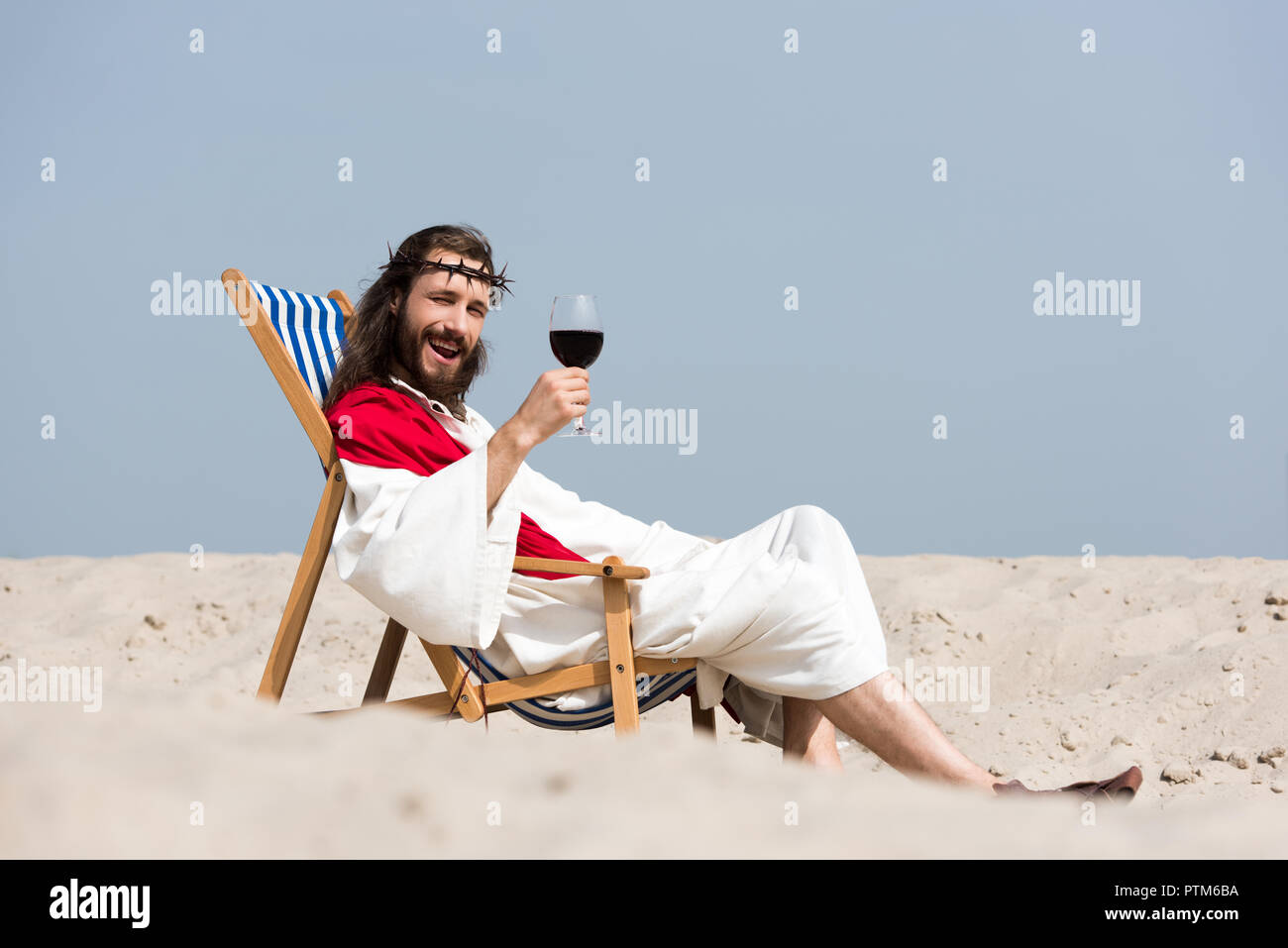 Jesús sonriente en túnica y fajín rojo descansando en las hamacas con una  copa de vino tinto en el desierto, mirando a la cámara Fotografía de stock  - Alamy