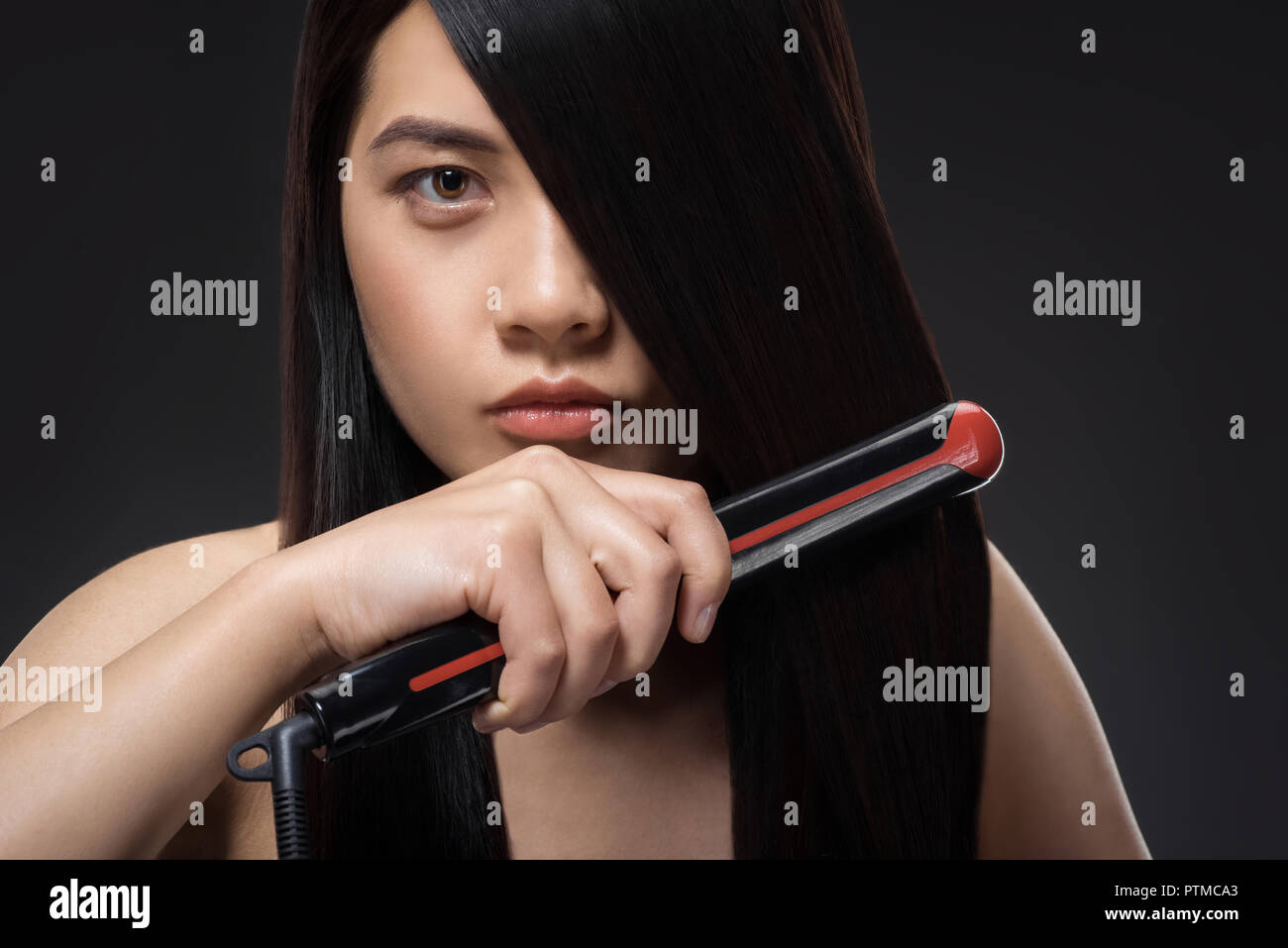 Retrato de joven mujer asiática el cabello liso con alisadores para el cabello aislado en negro Foto de stock