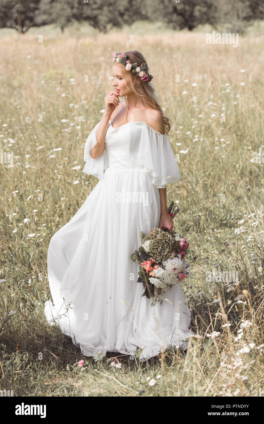 Hermoso vestido de novia novia pensativa y ofrenda floral sosteniendo  bouquet de flores en el campo Fotografía de stock - Alamy