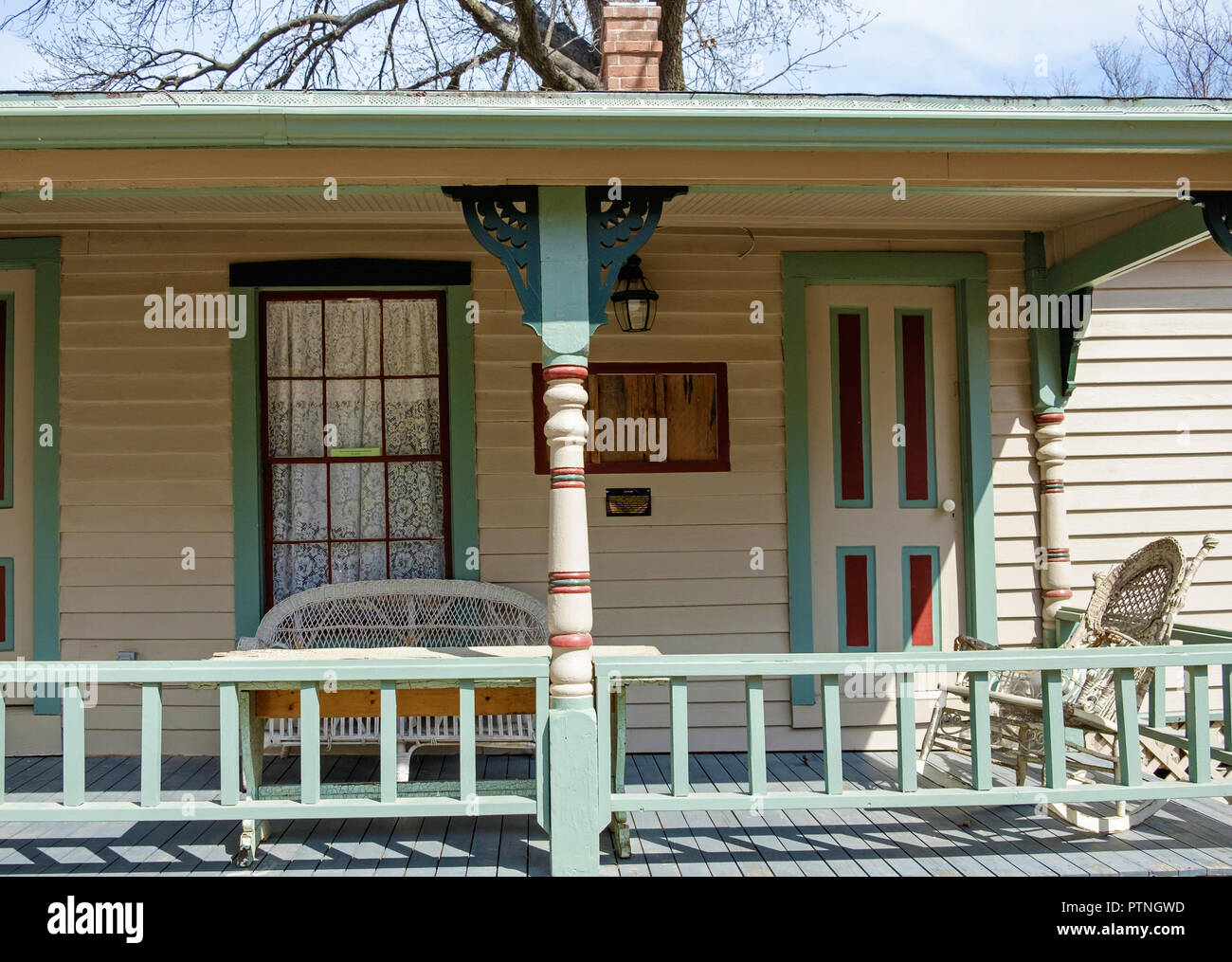 Porche cubierto en blanco shingled casa antigua con ribete azul. Silla mecedora, sofá de dos plazas. Dulaney Cottage, Castaños Square Historic Village, McKinney, Texas. Foto de stock