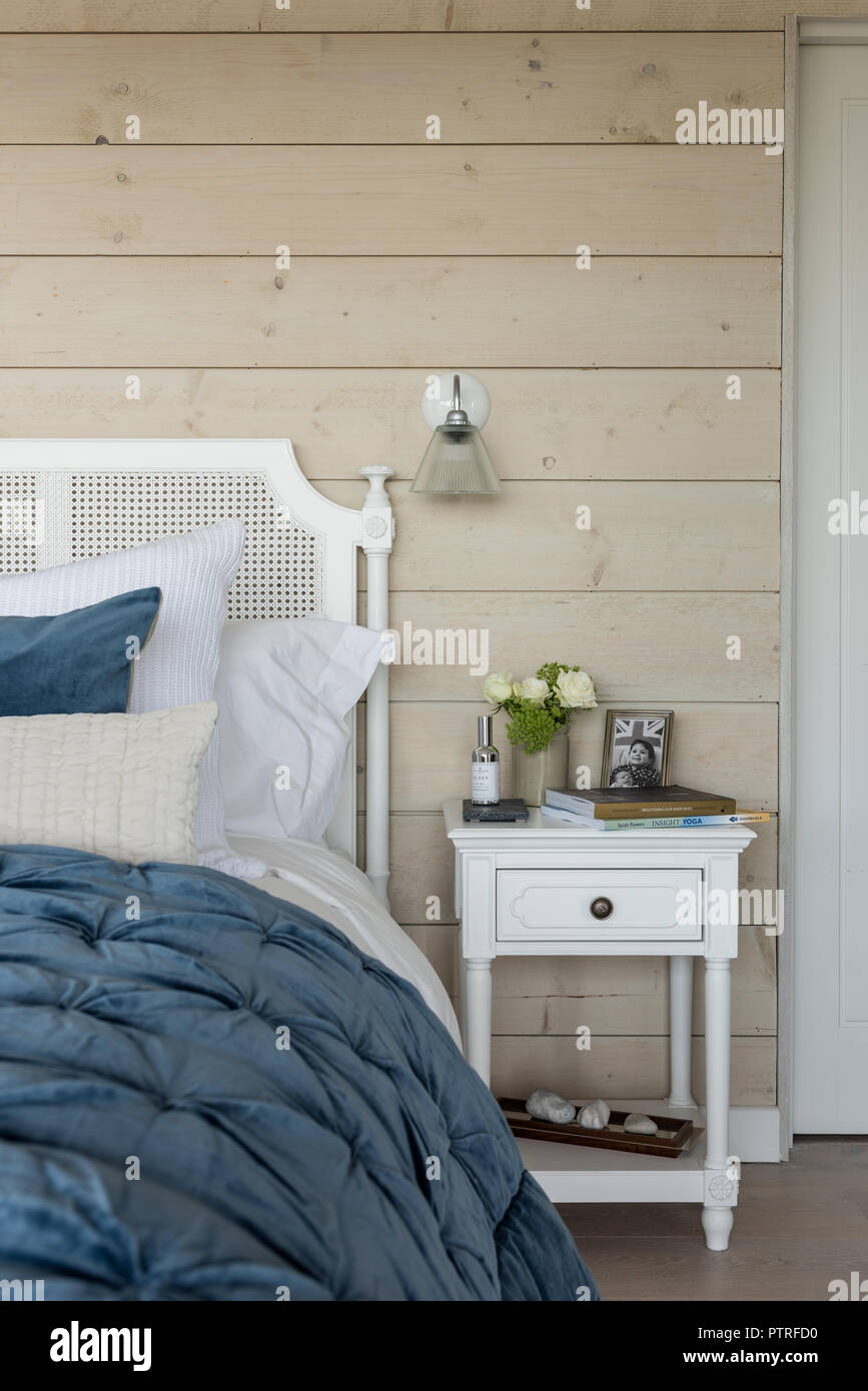Colcha azul en cama doble con revestimiento de madera y cristal de pared de luz Foto de stock