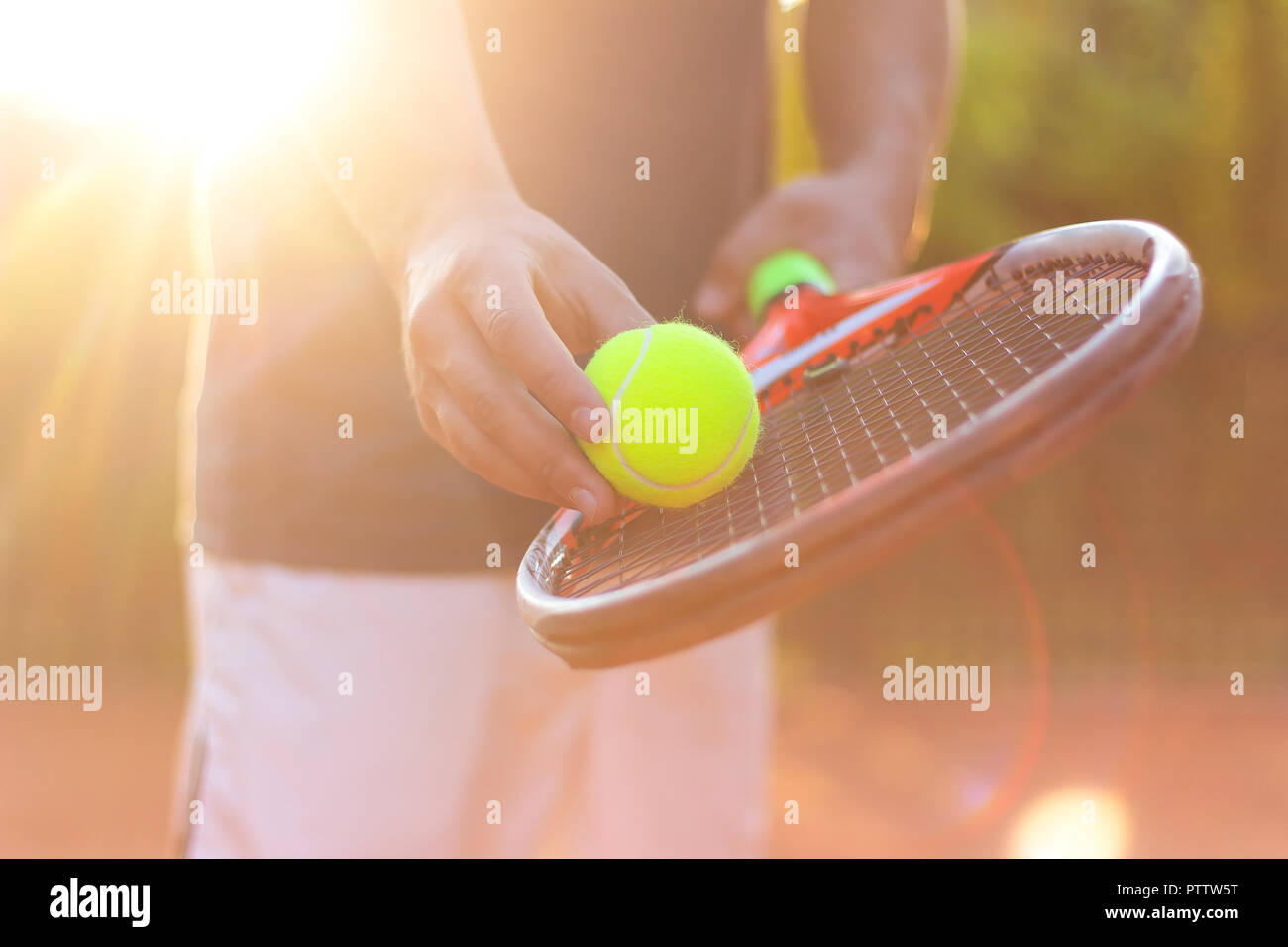 Un jugador de tenis se prepara para servir una pelota de tenis durante un partido con la luz del sol en segundo plano. Foto de stock