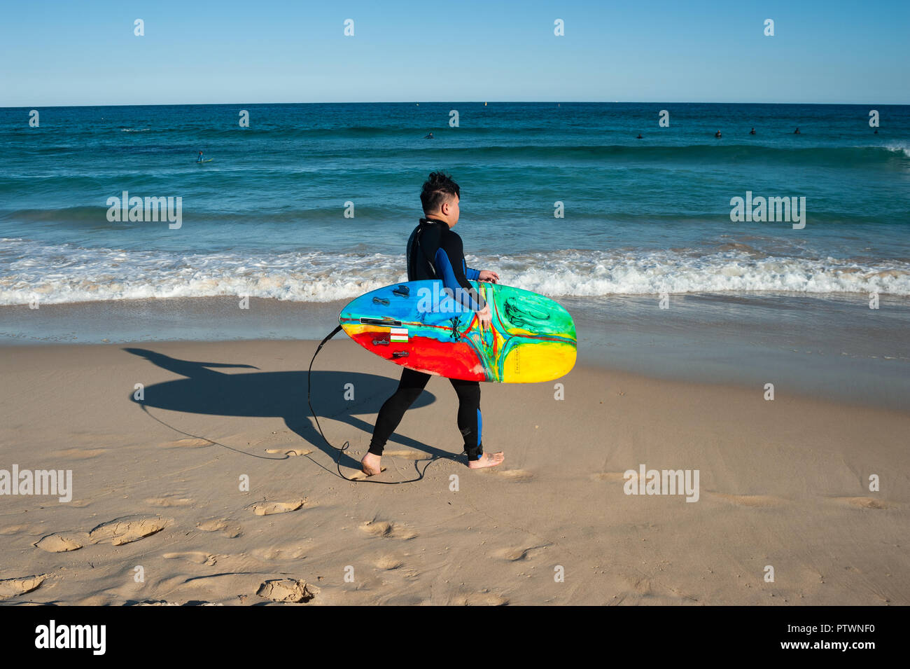 21.09.2018, Sydney, New South Wales, Australia - un surfista es visto sosteniendo su tabla de surf mientras camina hacia el mar en la playa de Bondi. Foto de stock