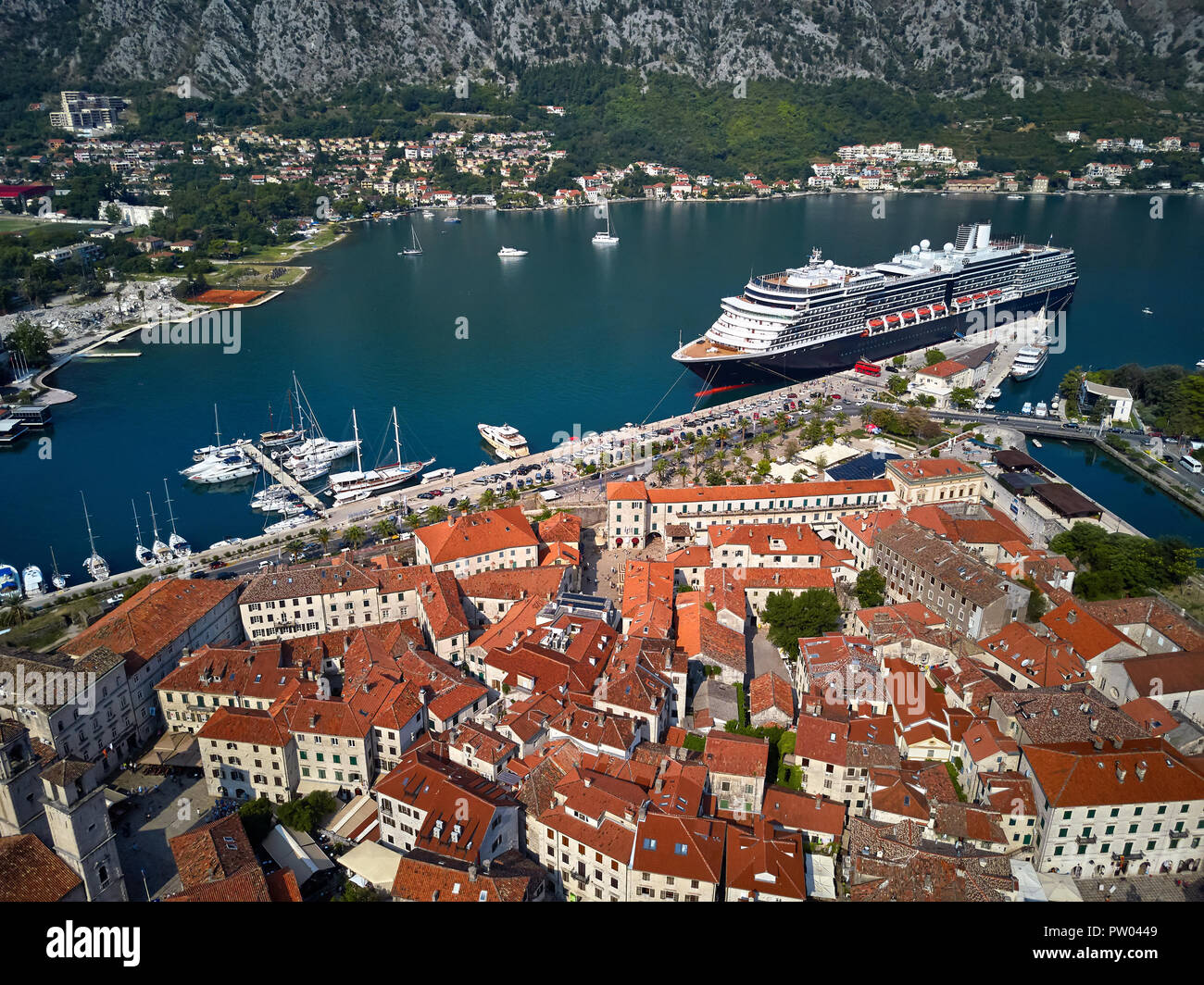 Crucero en un puerto de Kotor en Montenegro. En frente hay casas antiguas  con techos shingled rojo-naranja. Otros barcos y yates están en la se  Fotografía de stock - Alamy