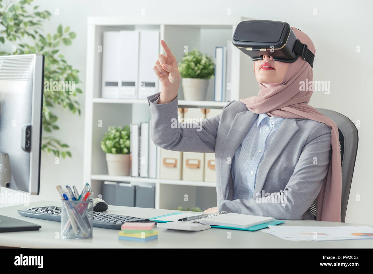 Elegante femenina musulmana tecnología VR personal que lleve gafas y apuntando su dedo en el aire para realizar un gráfico. Joven Empresaria con visor 3D y Foto de stock