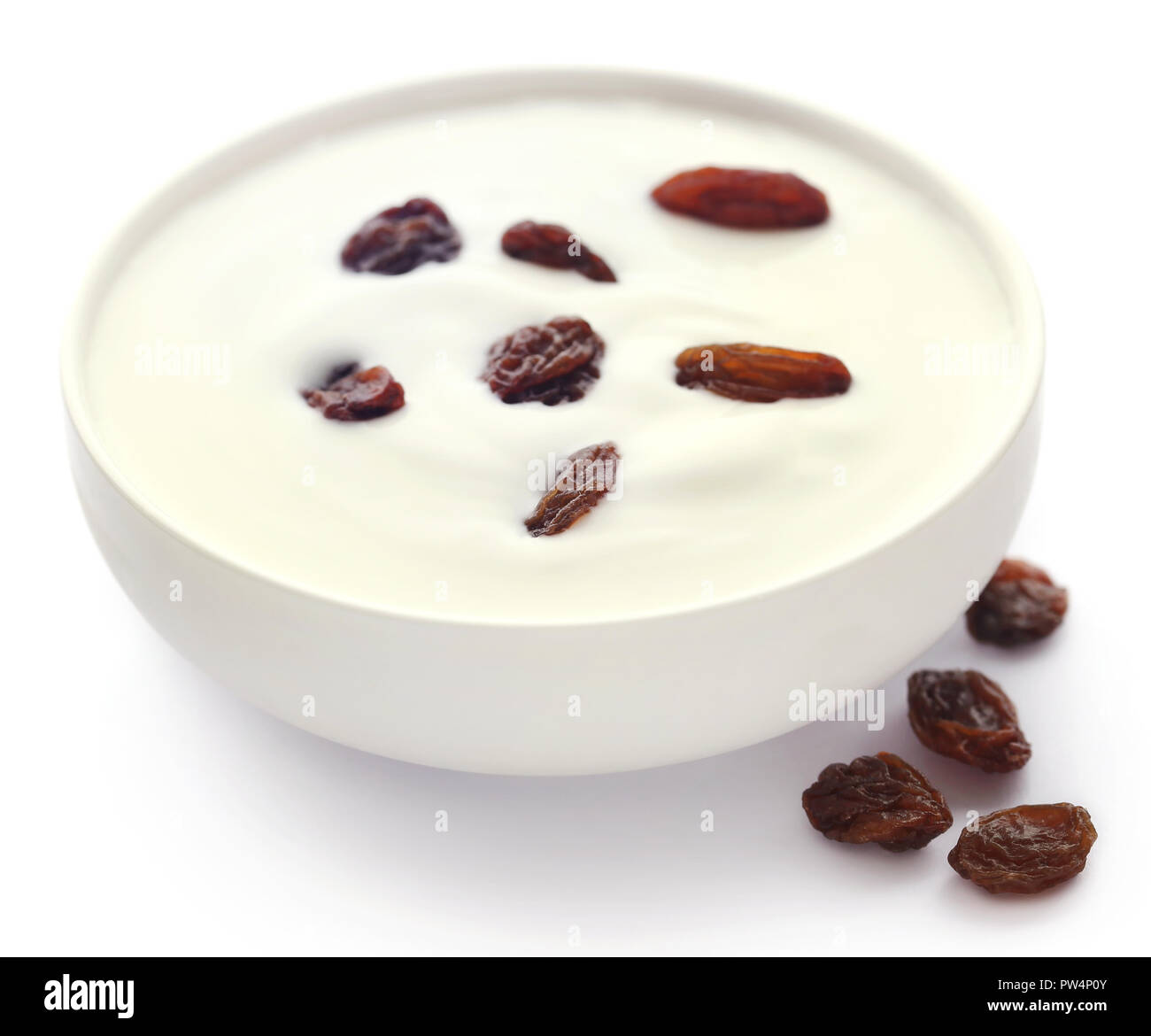 Yogur fresco en un recipiente con las pasas sobre blanco Foto de stock