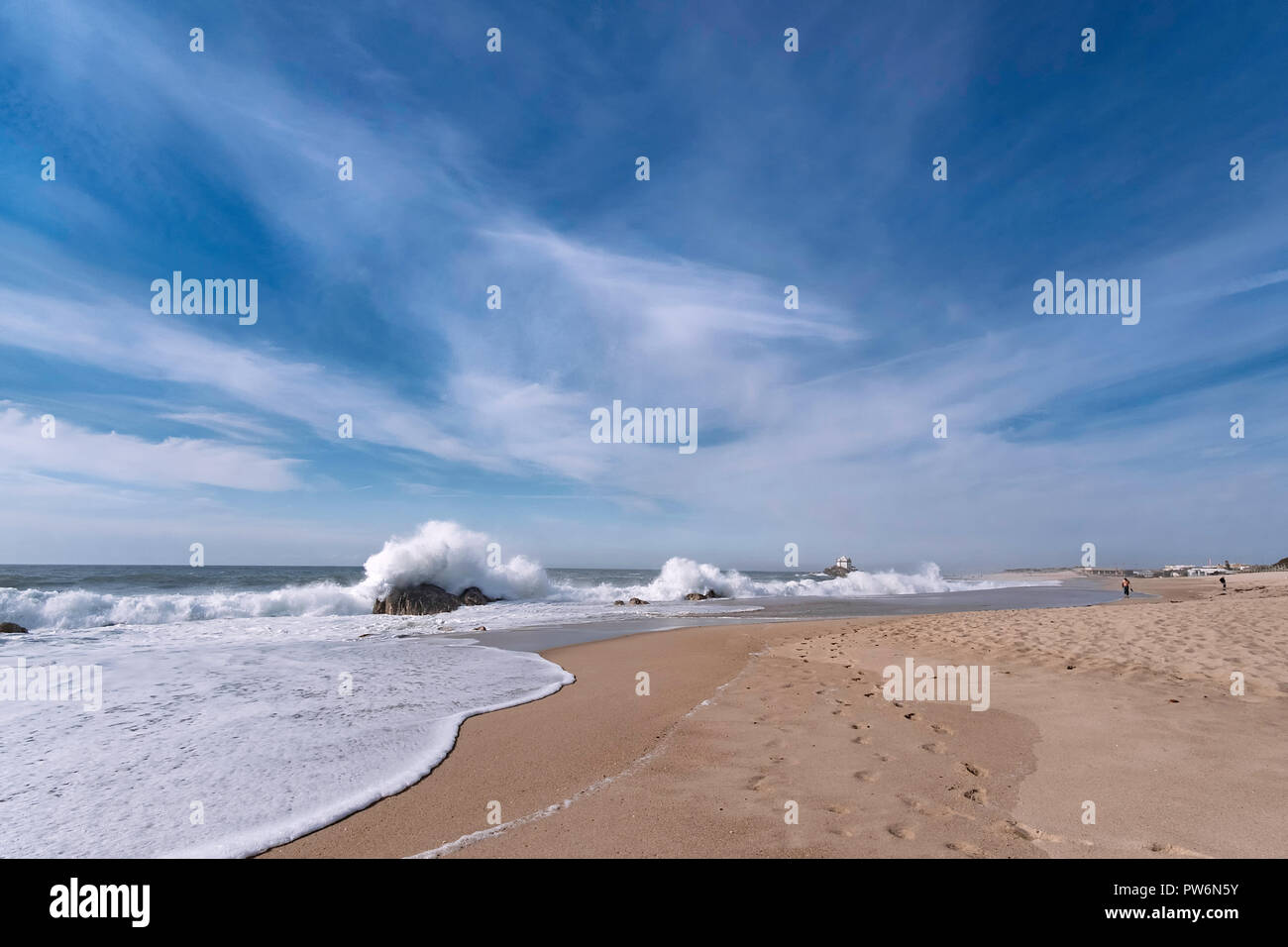 Paisaje de playa de arena, el cielo azul con algunas nubes, olas fuertes golpes contra las rocas a lo largo de la costa, un diente a una capilla en el extremo Foto de stock