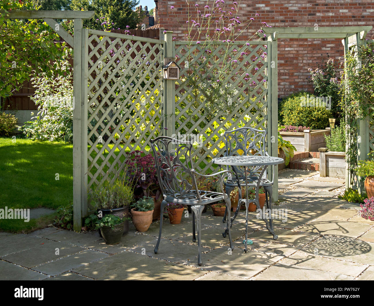 Jardín interno pequeño patio con mesa y sillas metálicas, losas de piedra natural y vigas pintadas Foto de stock