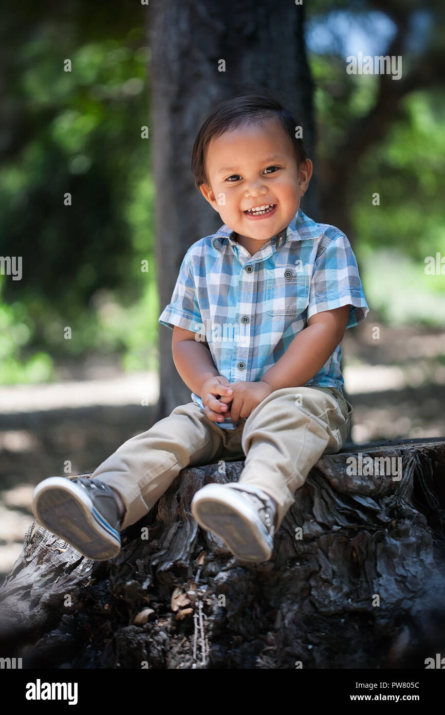Lindo chico mexicano con camisa de cuadros escoceses y una gran sonrisa saludable con los dientes del bebé sentados al aire libre durante el verano en el parque nacional de California Foto de stock