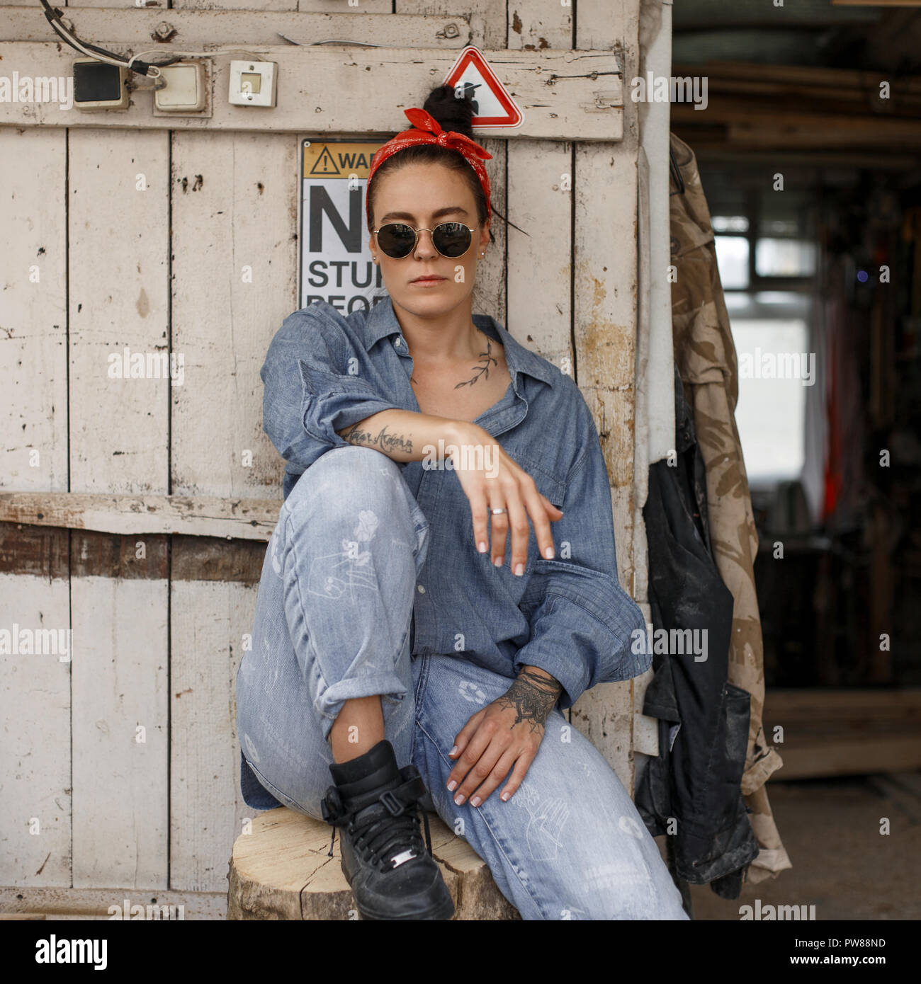 Estilo hipster Mujer con gafas de sol de moda en una moda denim camisa y  pantalones vaqueros sentados cerca de una pared de madera vintage  Fotografía de stock - Alamy