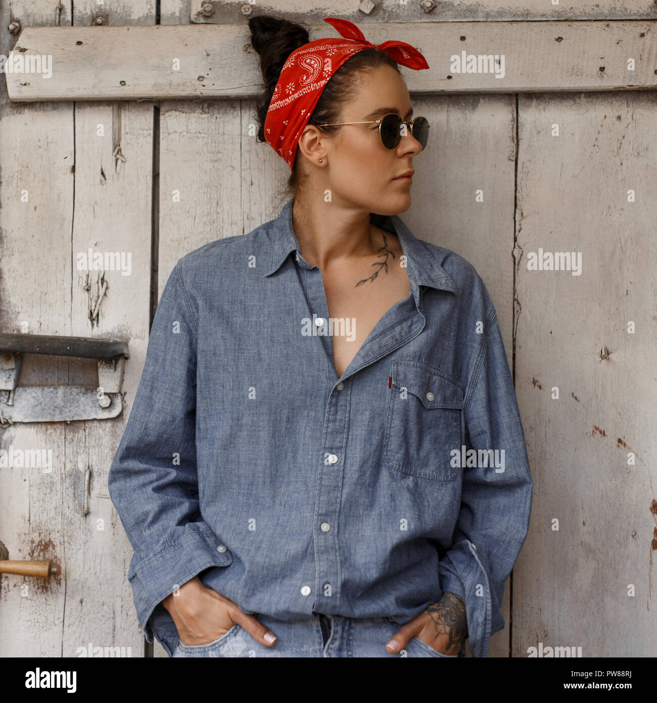 Bastante hipster Mujer con gafas de sol en moda y ropa denim blue jeans de  moda está cerca de una pared de madera vintage Fotografía de stock - Alamy