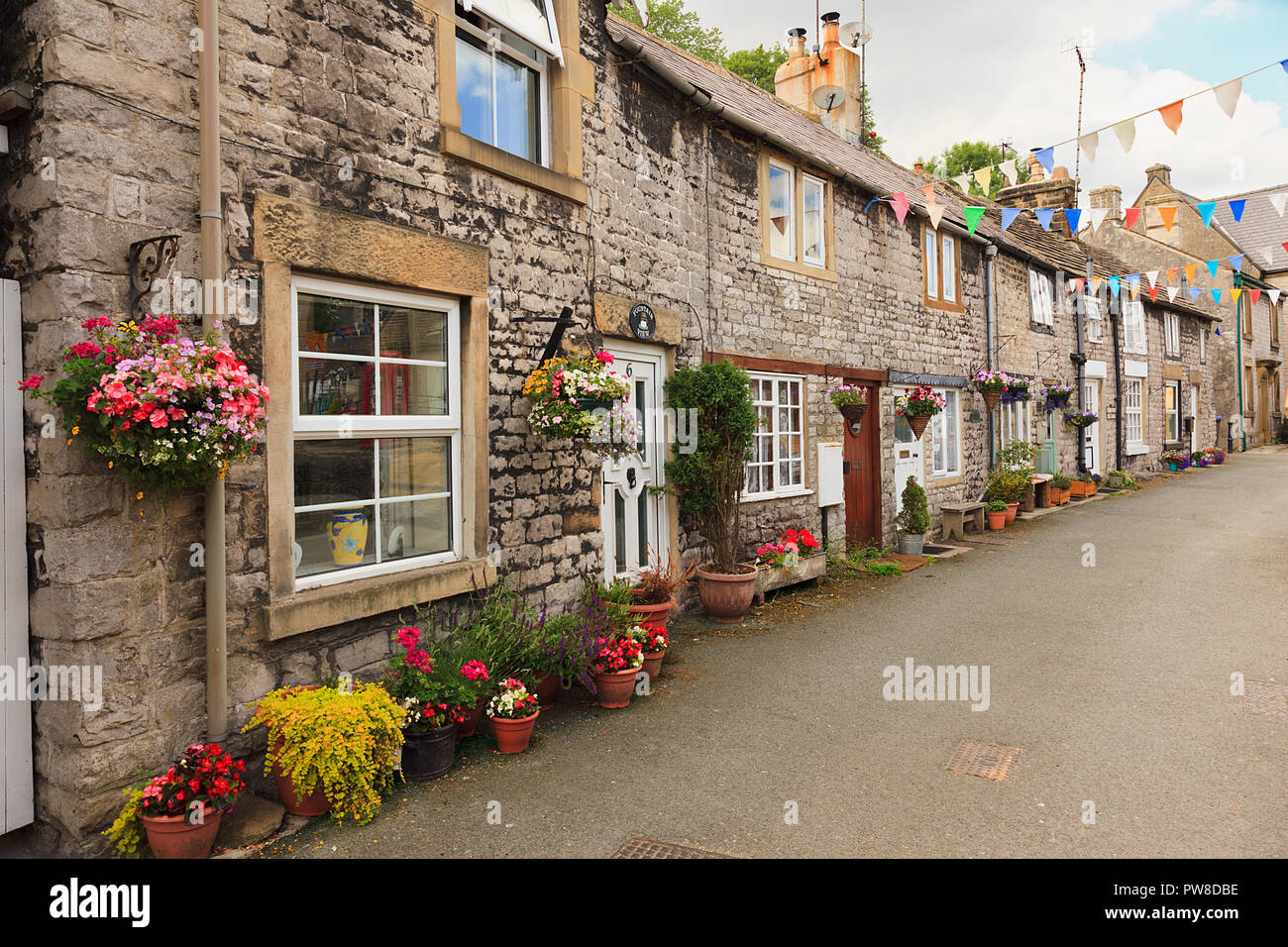 Calle de coloridas casitas de piedra de época con cestas colgantes y macetas muestra en Tideswell Derbeyshire Dales UK Foto de stock