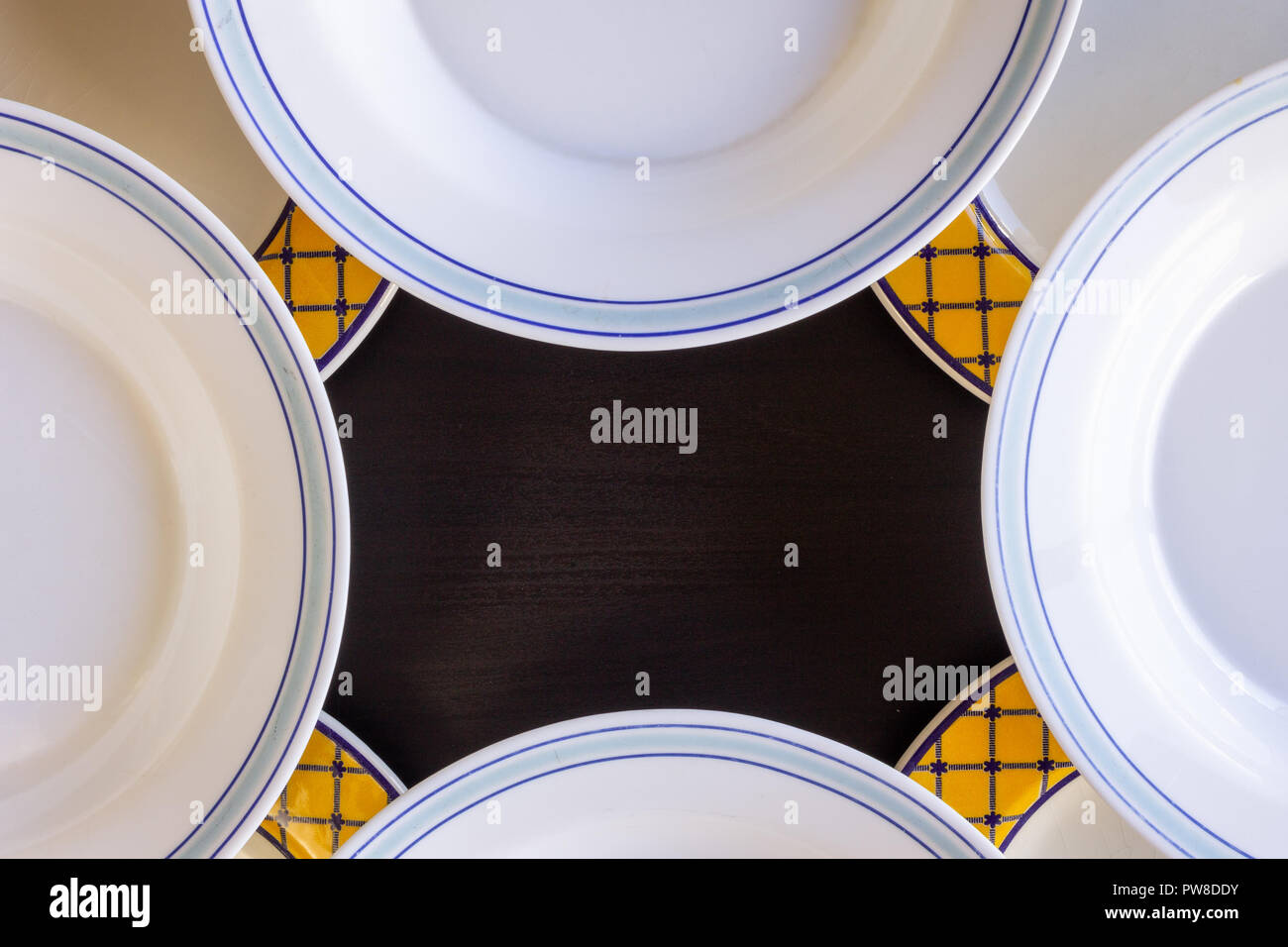 https://c8.alamy.com/compes/pw8ddy/un-fondo-de-madera-negra-con-cuatro-platos-vacios-en-blanco-y-amarillo-y-azul-y-blanco-de-cuatro-platos-vacios-pw8ddy.jpg
