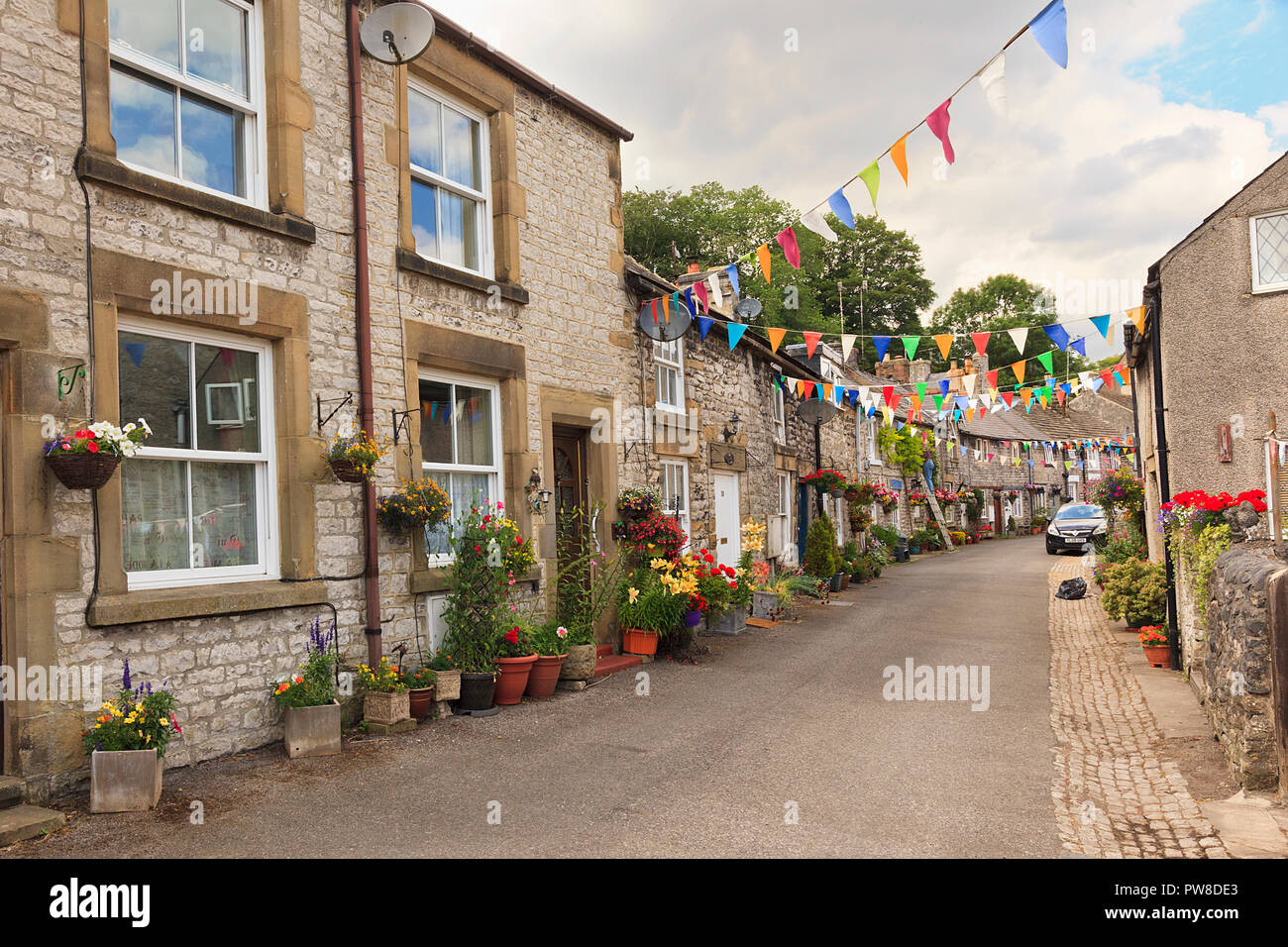 Calle de coloridas casitas de piedra de época con cestas colgantes y macetas muestra en Tideswell Derbeyshire Dales UK Foto de stock