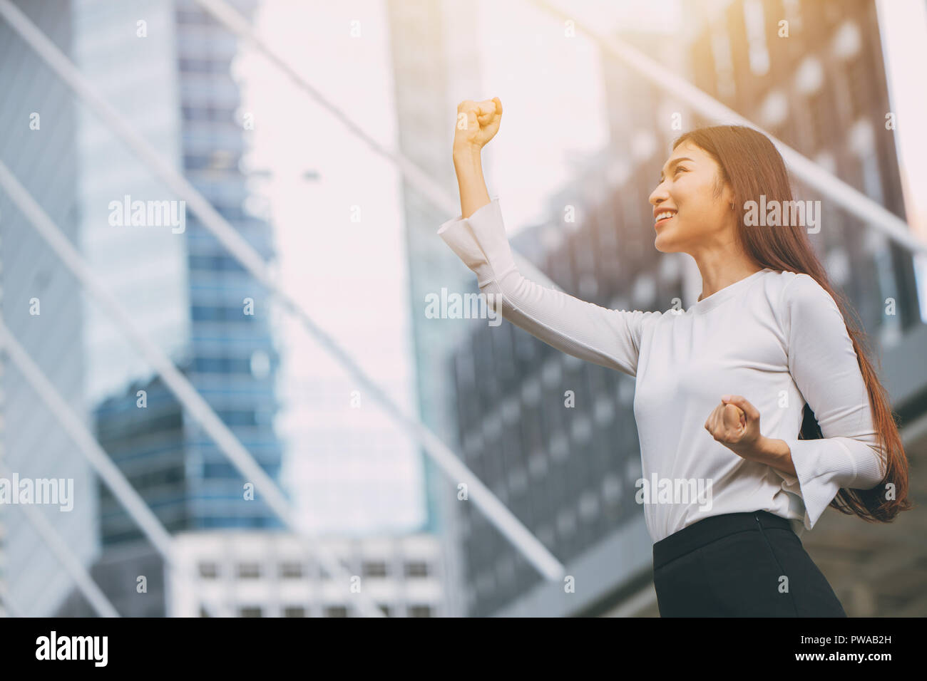 Ganador exitoso negocio empleado chica puño levantan la mano con edificios de oficinas de la ciudad de fondo Foto de stock