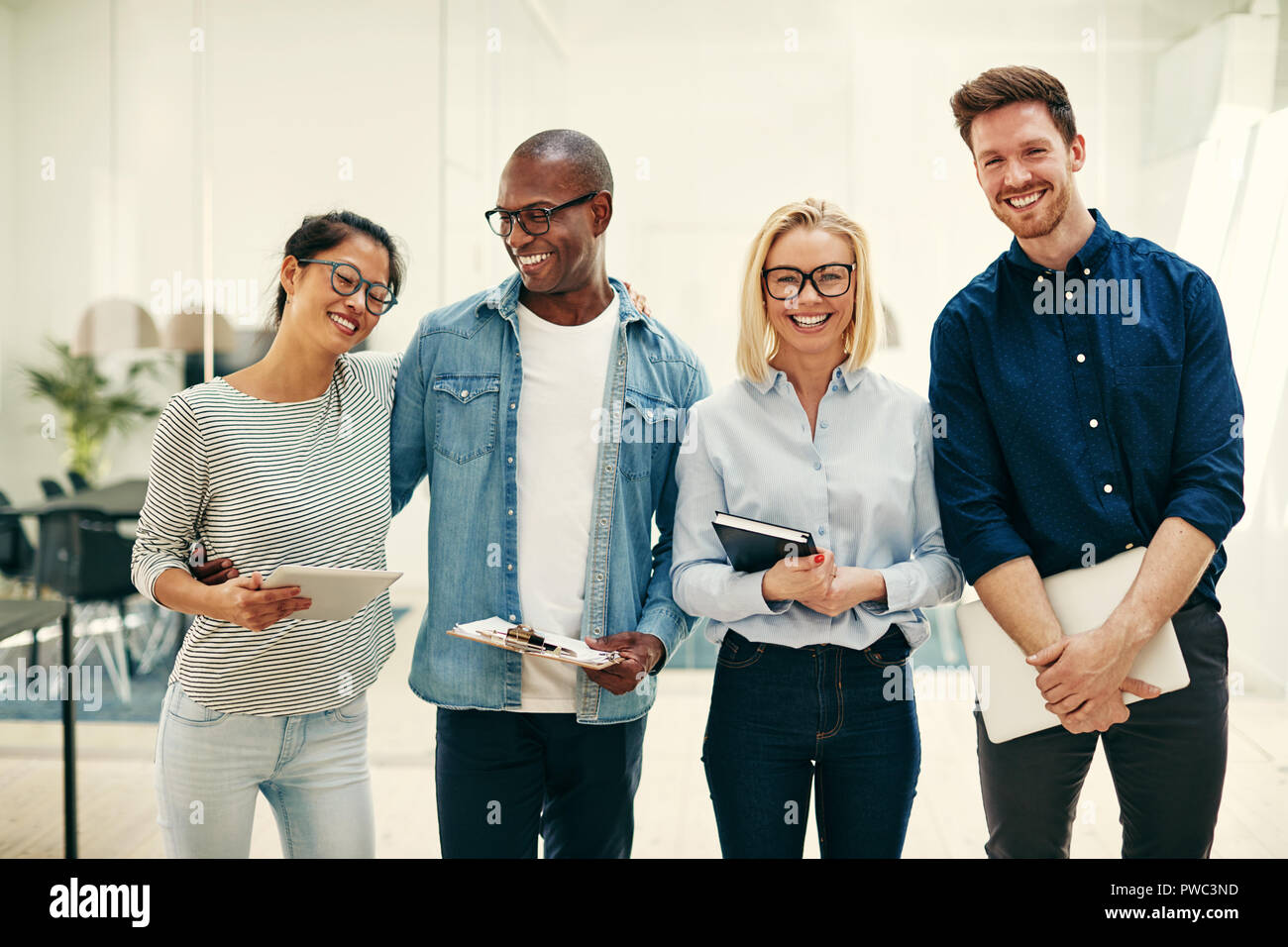 Laughing grupo diverso de jóvenes empresarios que trabajan codo con codo junto en una luminosa oficina moderna Foto de stock