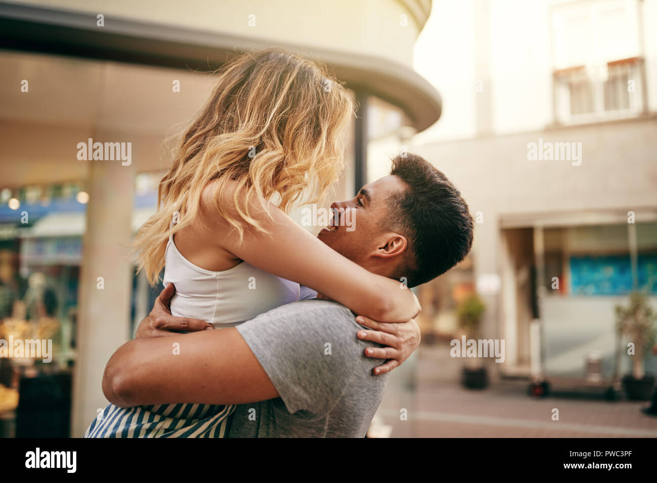 Pareja joven abrazando y mirándose a los ojos mientras se comparte un momento romántico en una calle de la ciudad Foto de stock
