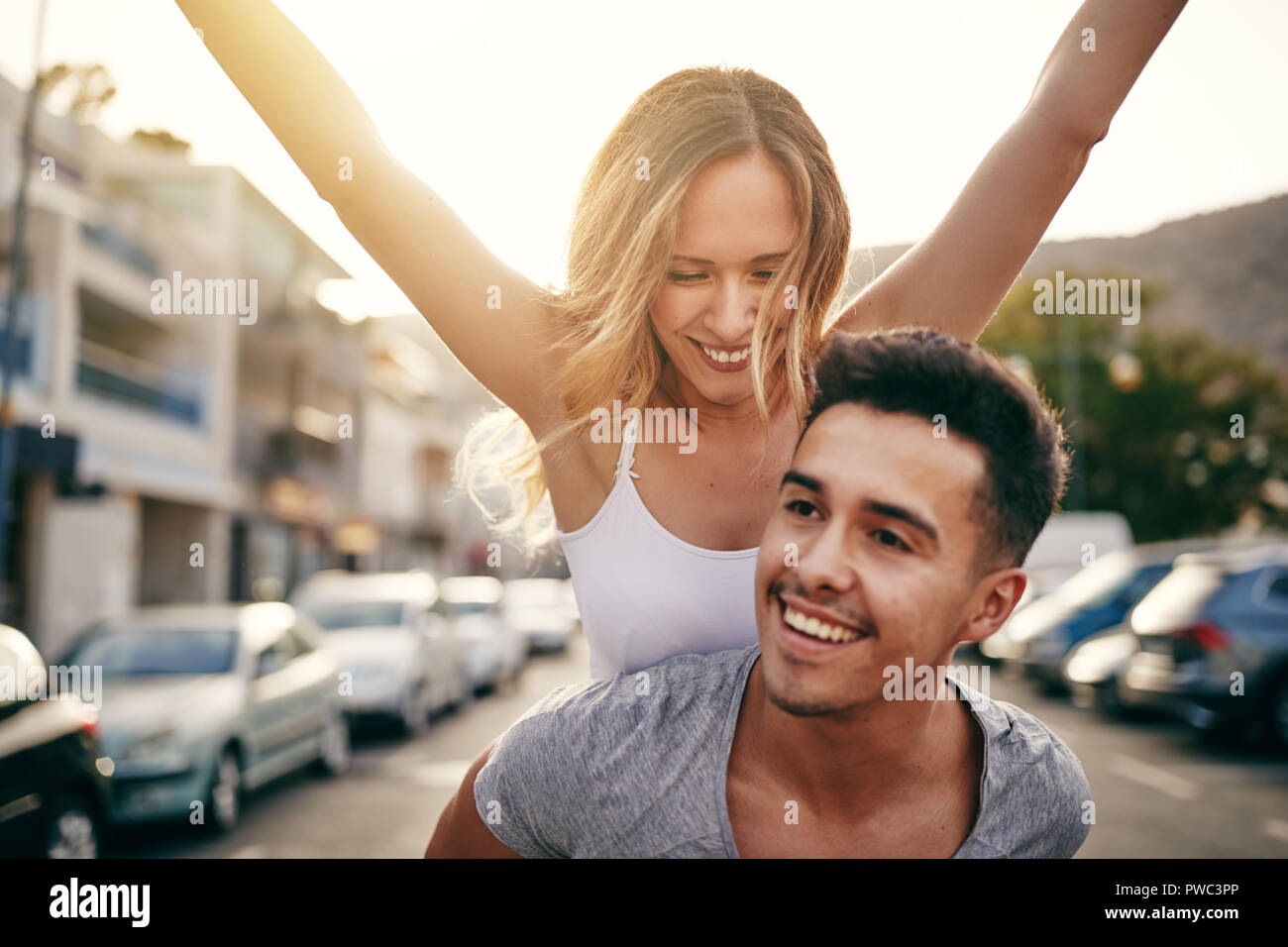 Laughing joven con sus brazos levantados siendo transportada sobre los hombros de su novio por las calles de la ciudad Foto de stock