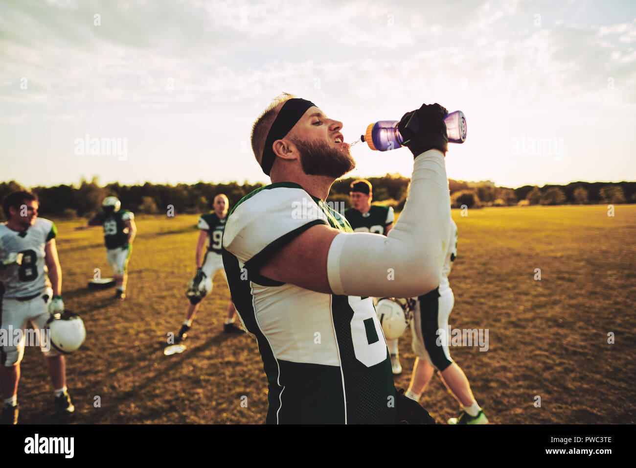 Jugador de fútbol americano de una botella de agua potable mientras está de pie en un campo durante una práctica del equipo Foto de stock
