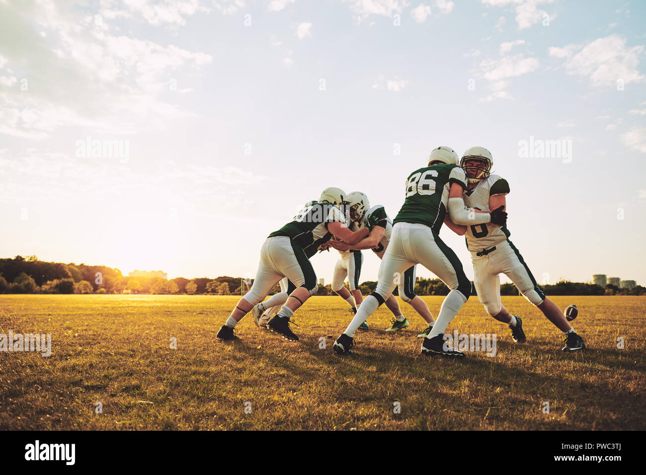 Grupo de jóvenes jugadores de fútbol americano practicando ejercicios ofensivos y defensivos en un campo de deportes en una tarde soleada Foto de stock