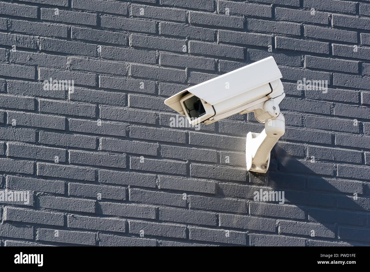 Ver en una cámara de vigilancia blanca colgando en lo alto de una pared de ladrillo gris. La cámara está colgando para fines de prevención y seguridad. Foto de stock