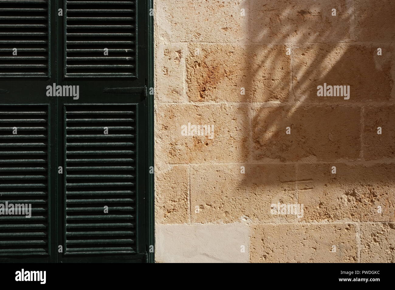 Obturador de madera y fuerte sombra proyectada en la pared de piedra Ciutadella Menorca España Foto de stock