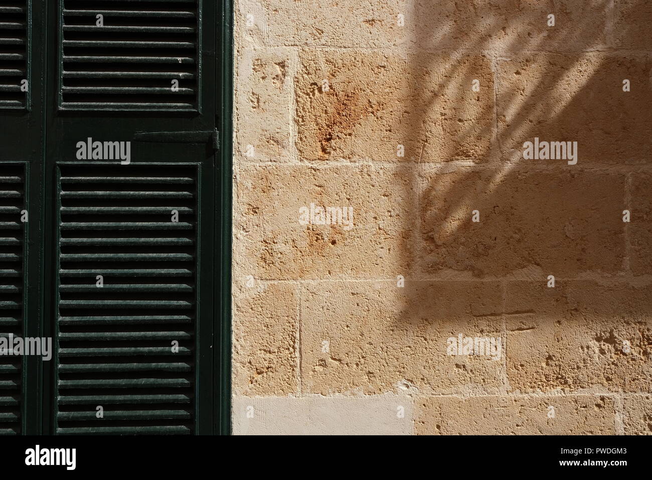 Obturador de madera y fuerte sombra proyectada en la pared de piedra Ciutadella Menorca España Foto de stock