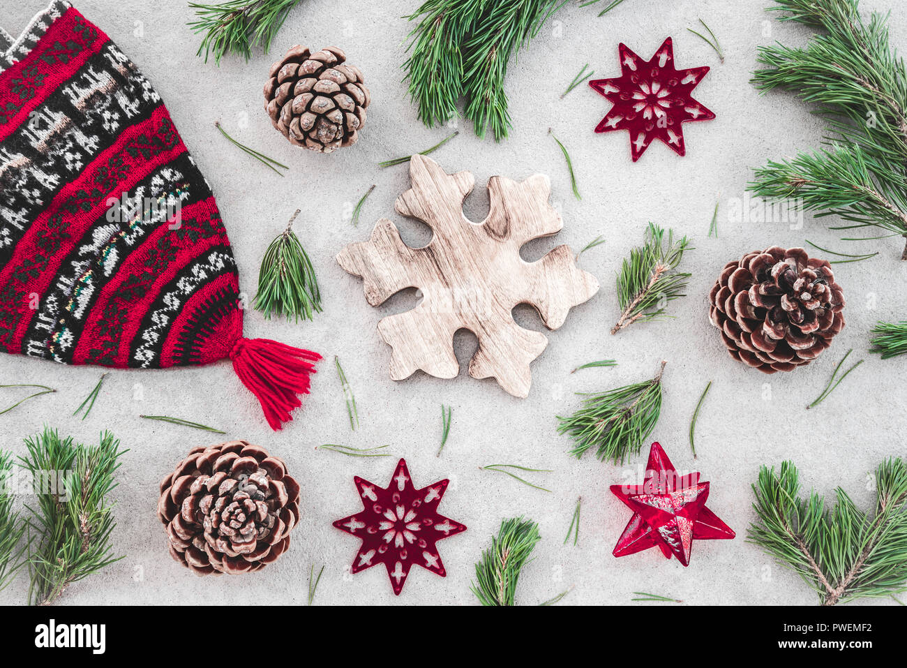 Decoración de Navidad de estilo nórdico. Sombrero de invierno tejido rojo, verde ramas de pino, conos y estrellas, sobre fondo de hormigón. Foto de stock
