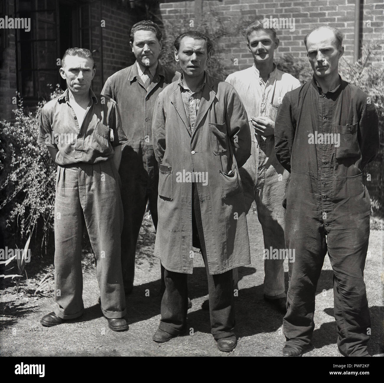 1950, un grupo de trabajadores de la fábrica de neumáticos británica en su  ropa de trabajo o monos están fuera de la oficina de la empresa para una  imagen, Inglaterra, Reino Unido