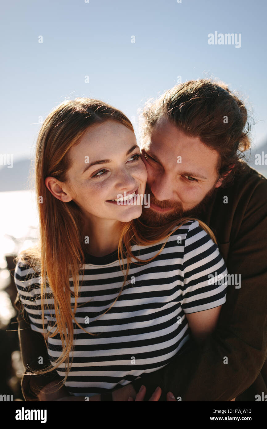 El hombre abrazando a la mujer desde atrás en la playa. Pareja en un ambiente romántico y felices disfrutando de unas vacaciones. Foto de stock