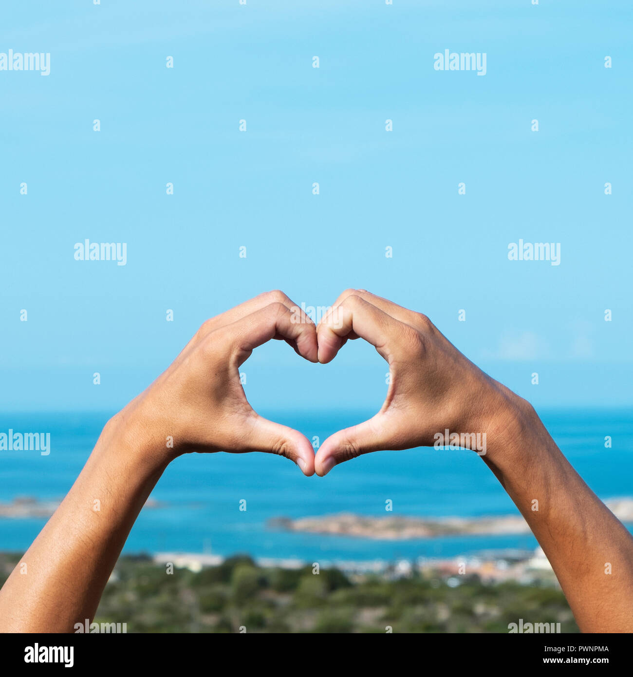 Primer plano de las manos de un joven hombre caucásica formando un corazón en frente del mar en la costa sur de Córcega, en Francia Foto de stock