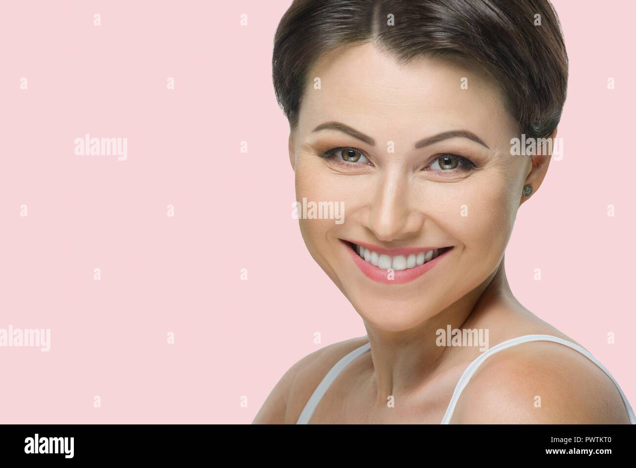 Mujer morena madura positiva con sonrisa blanca estrecha sobre fondo de  color rosa pastel Fotografía de stock - Alamy
