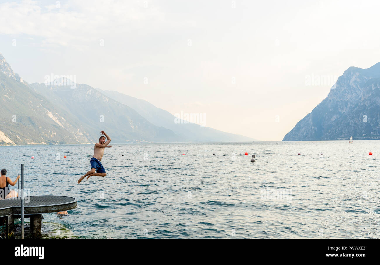 Apuesto hombre atractivo divertido divertirse saltando en el agua en el Lago di Garda en Italia en el verano de vacaciones divertidas vacaciones viajes alrededor de Europa. Foto de stock