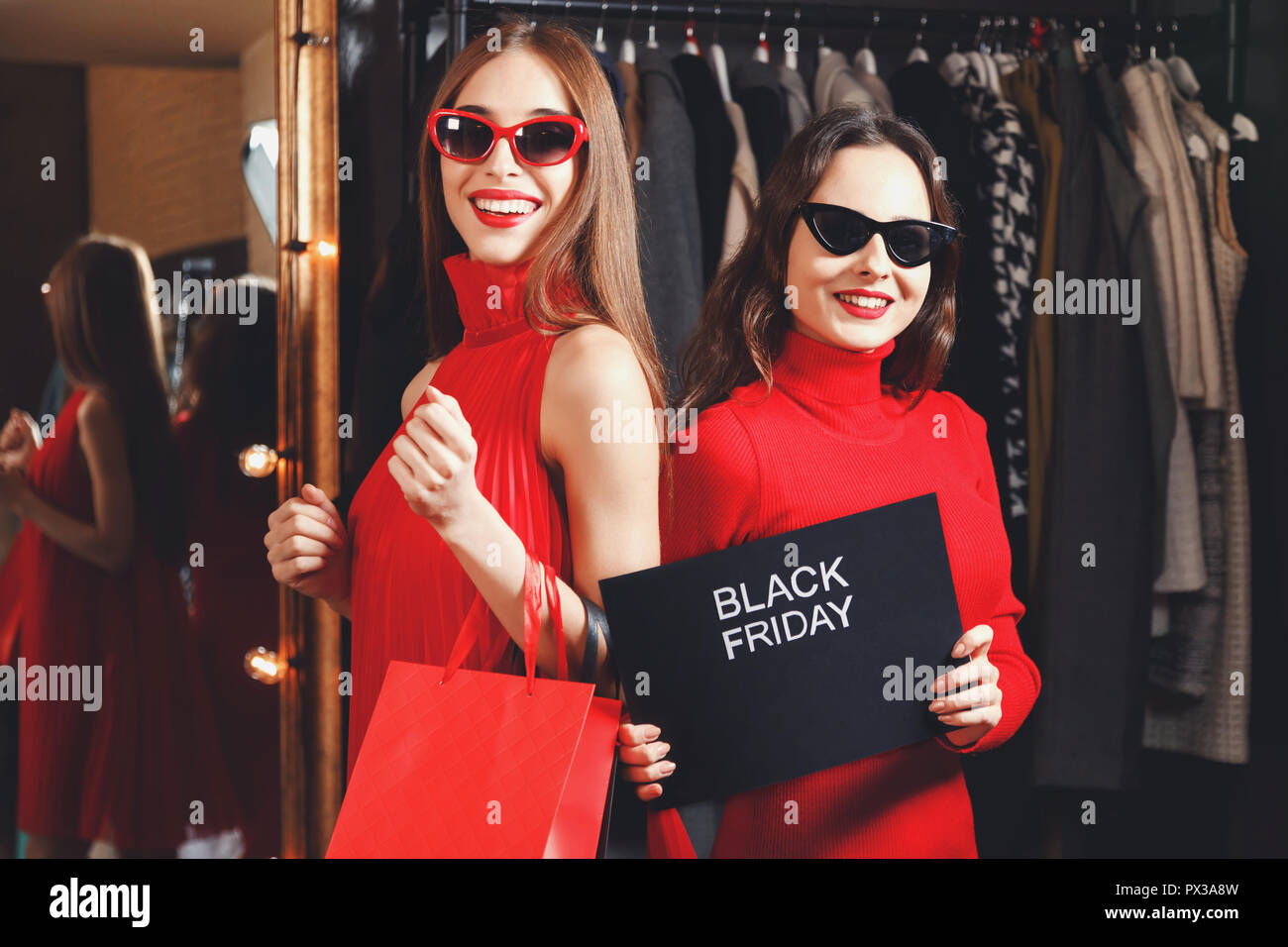 Feliz éxito alegres chicas con gafas de sol y vestidos rojos celebración  viernes negro tarjeta en Fashion Mall durante el proceso de compra,  concepto de consumismo, Black Friday, la venta, la rica