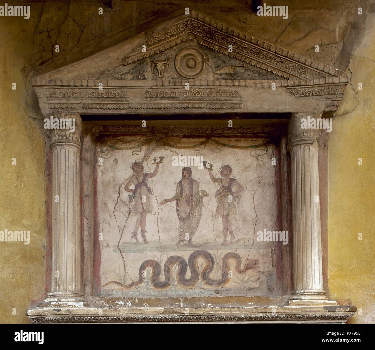 Pompeya. Casa de los Vettii. Lararium. Dos Lares, sosteniendo un rhyton, flanquean un genio con un tazón de libación y caja de incienso, su cabeza cubierta por un sacrificio. La serpiente, asociada a la prosperidad, los enfoques de un altar. El tímpano muestra una patera, un cráneo de buey y un cuchillo de sacrificio. Italia. Foto de stock