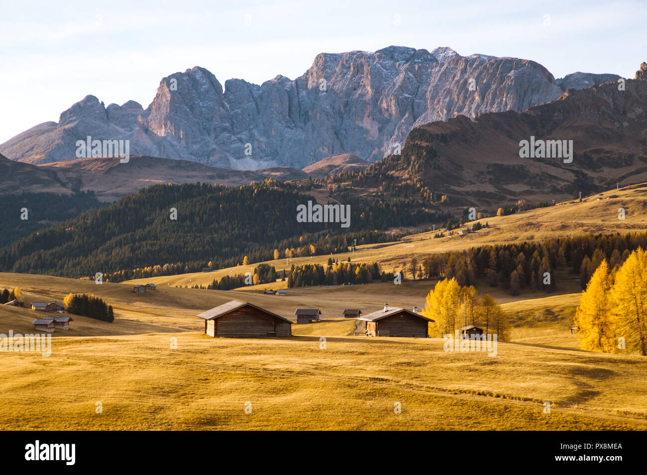 Hermosa vista de madera tradicionales chalets de montaña en el Scénic Alpe di Siusi con famosos Langkofel picos de montañas en el fondo en la mañana de oro Foto de stock