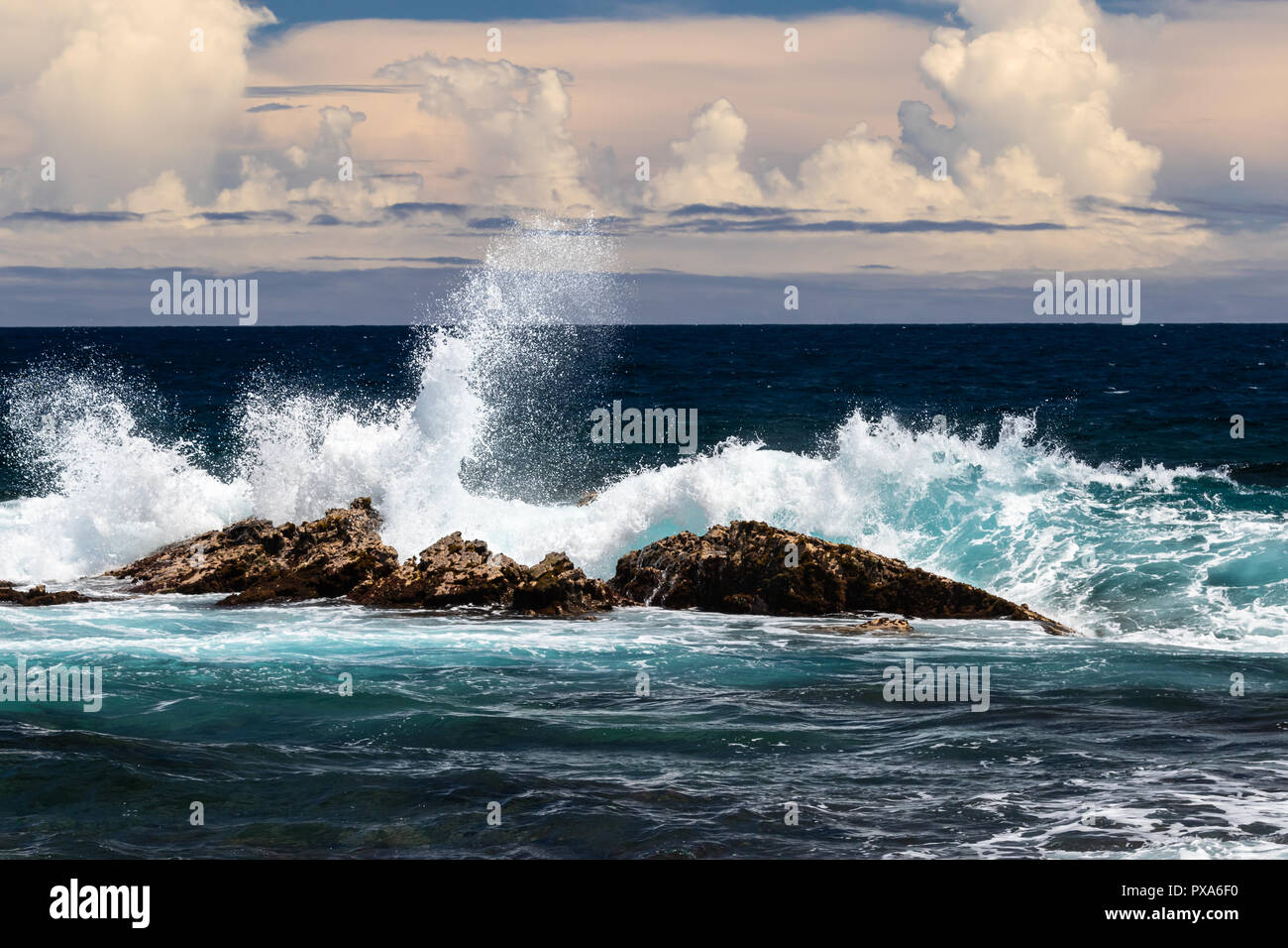 Ola rompiendo en roca oscura; blanco spray en el aire, onda a un lado oscuro y nubes en el fondo del océano. Playa de arena negra, Punaluu, Hawai. Foto de stock